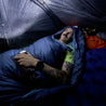 Alpin Loacker sininen ultrakevyt makuupussi, mies telttailee teltassa ultrakevyen makuupussin kanssa 3 vuodenaikaa